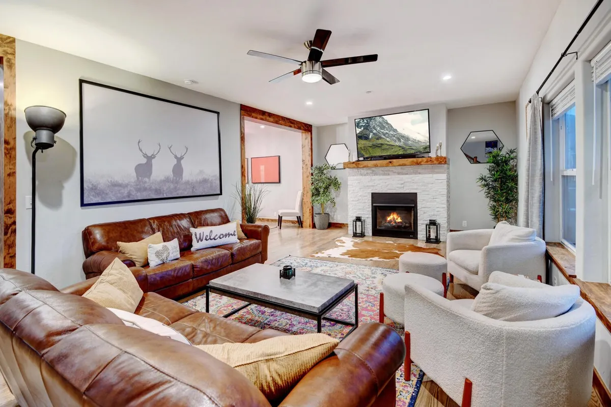 The image showcases a luxurious, open-concept living room with a crackling fireplace as the central focus, surrounded by plush leather sofas and elegant décor. Warm lighting, inviting textures, and tasteful artwork create a cozy ambiance perfect for relaxing, gathering with friends or family, and enjoying tranquil evenings indoors.