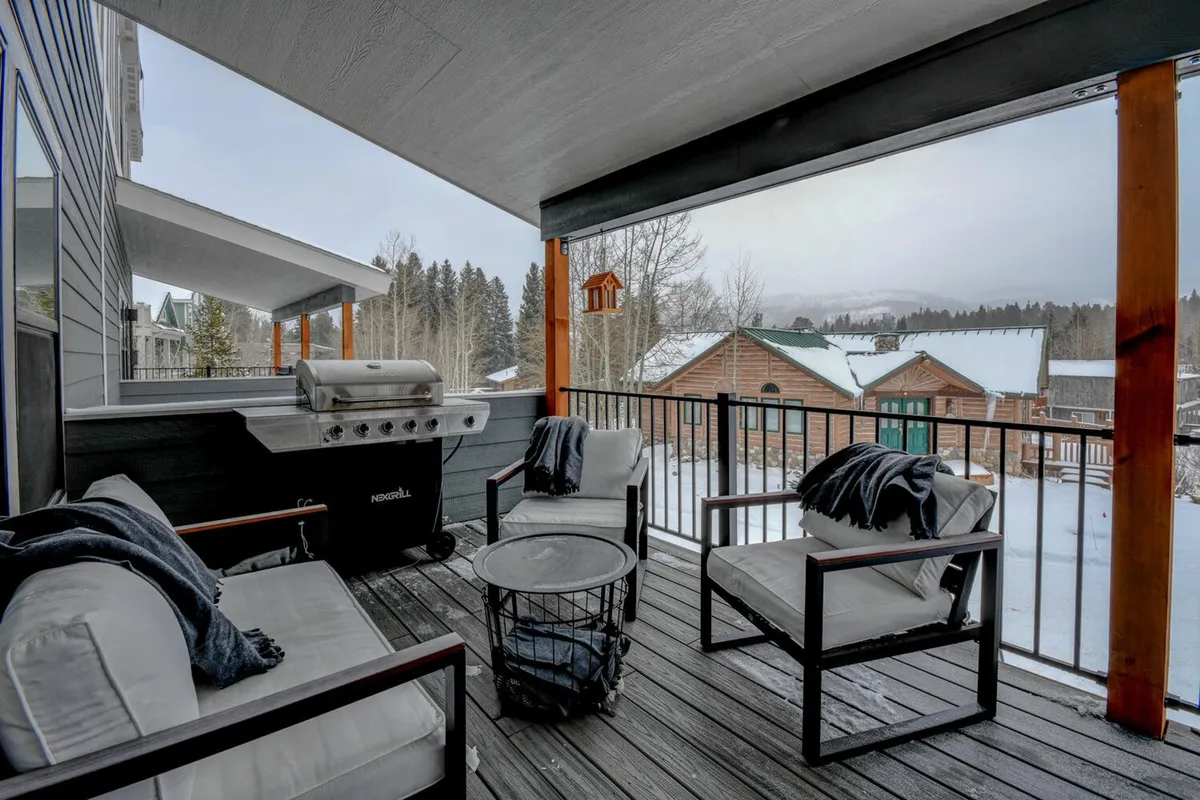 An exterior deck scene with an outdoor seating area, gas grill, snow-covered landscape, and trees. The arrangement invites outdoor dining and relaxation, extending the social experience beyond the kitchen and dining area.