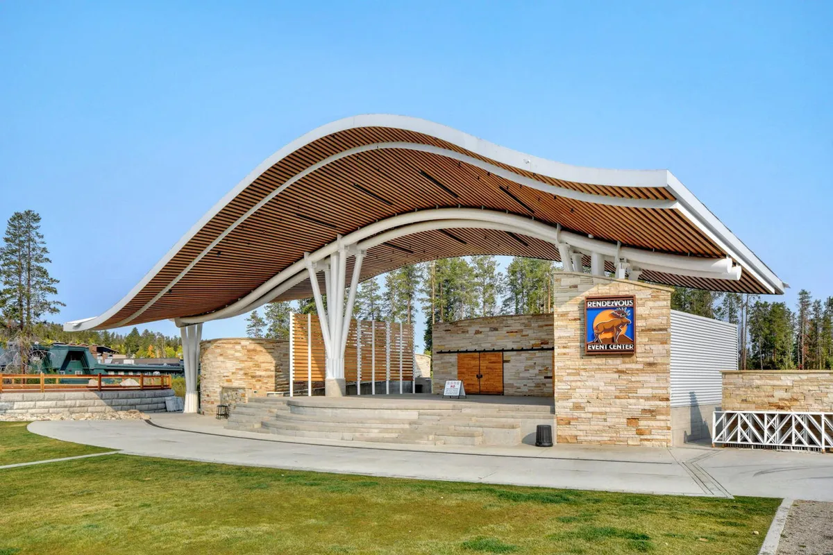 An inviting outdoor stage area framed by a curved roof and stone walls, set up for concerts or community events. The open-air setting suggests a place for lively gatherings, summer festivals, and memorable moments with family.