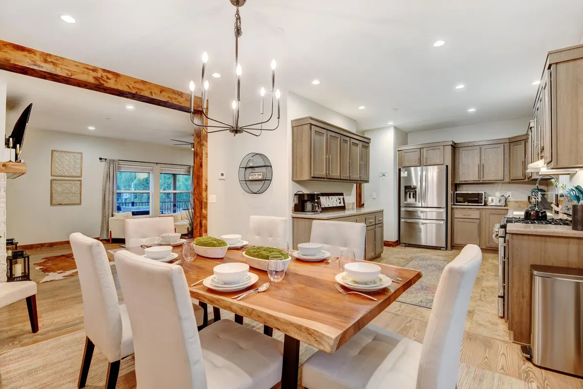 A dining area with a large table elegantly set, chandelier lighting, and cabinetry in the background, opening fluidly to the kitchen. The inviting setup is perfect for group meals and celebrations.