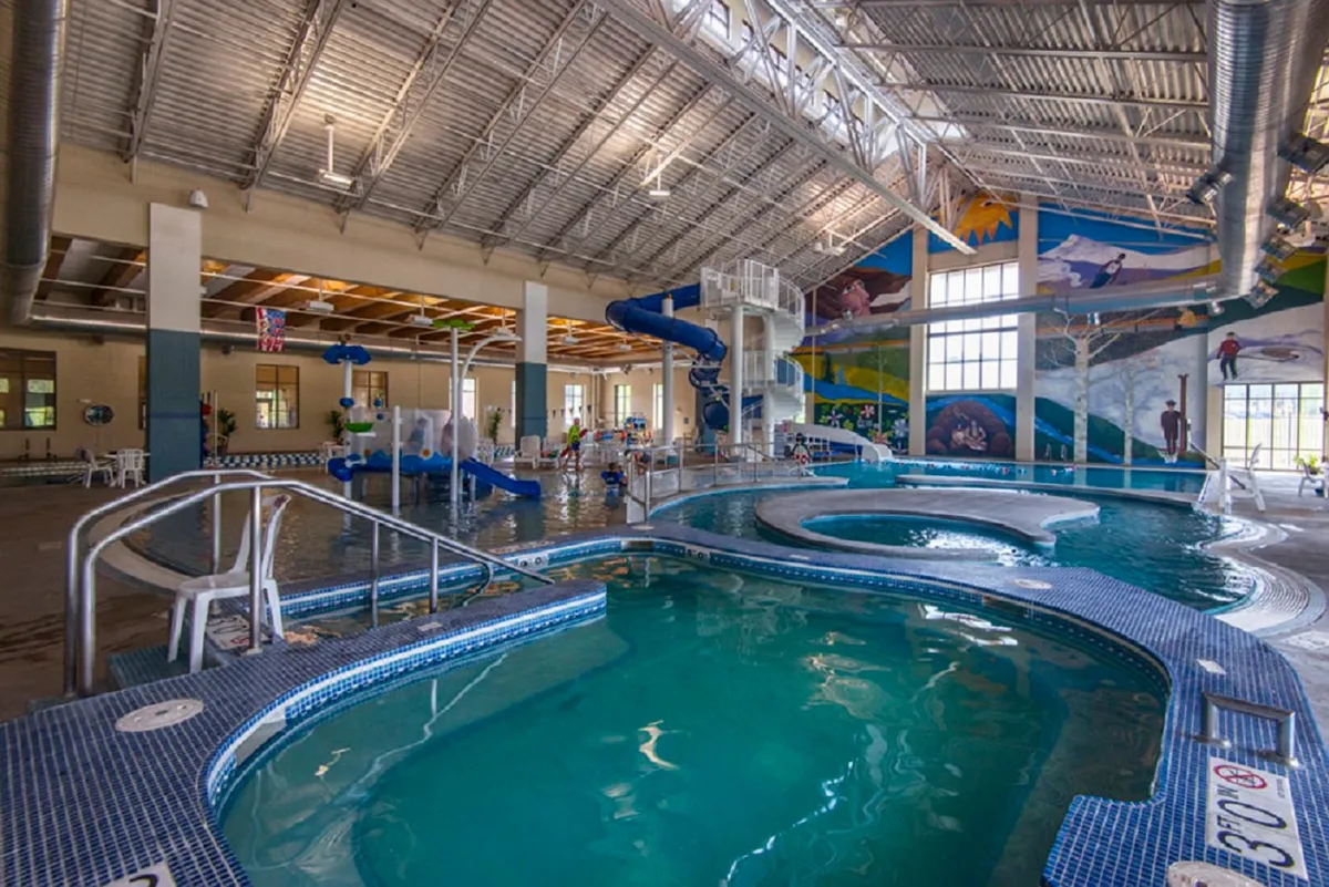 A lively indoor pool area with colorful water slides and murals, bustling with children playing and families relaxing. The vibrant energy in the scene conveys the joy of shared activities and family fun, echoing the variety of complimentary resort experiences available in different seasons.