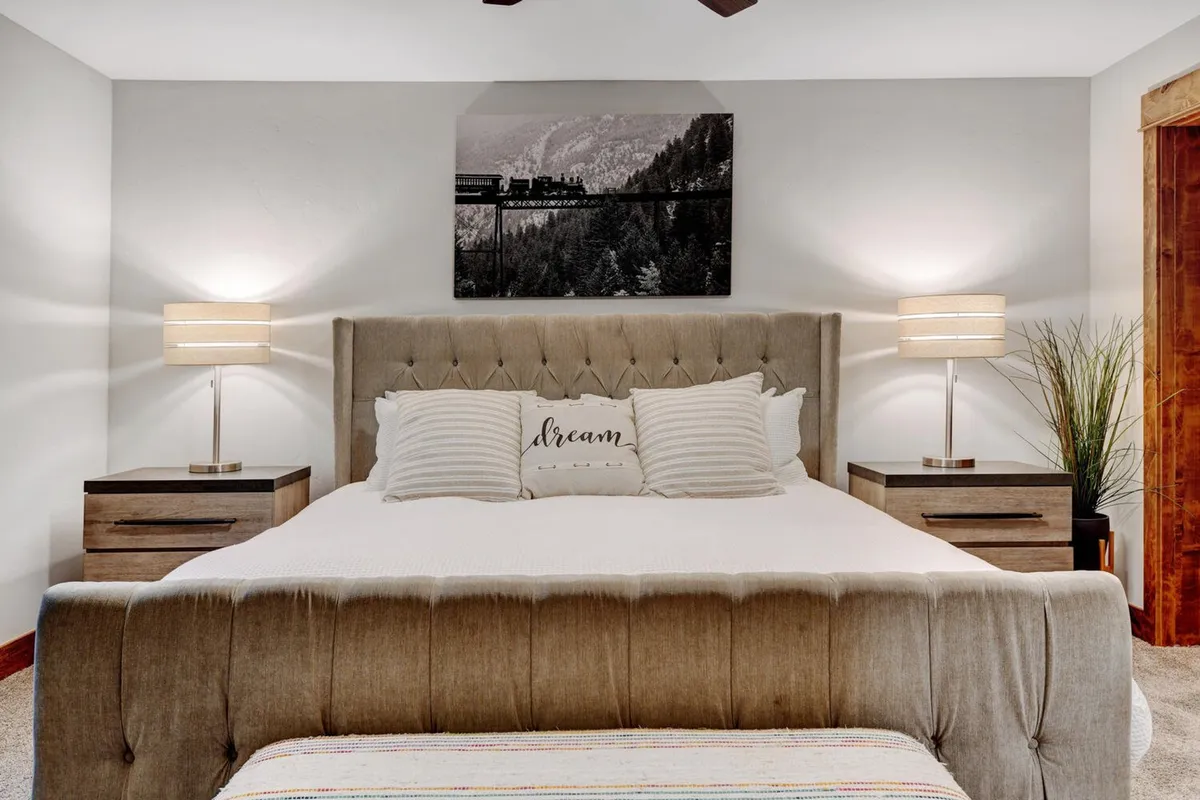 A serene bedroom featuring a bed with a tufted headboard, decorative pillows, soft lighting from bedside lamps, and tasteful artwork on the wall, all creating a calming, retreat-like atmosphere.