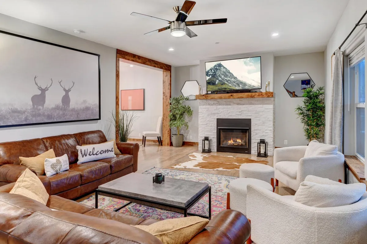 A cozy living room with a leather sofa, fireplace, TV above the mantel, artwork featuring deer, and an area rug. The atmosphere is warm, perfect for relaxing after a day of adventure or gathering for a movie night.