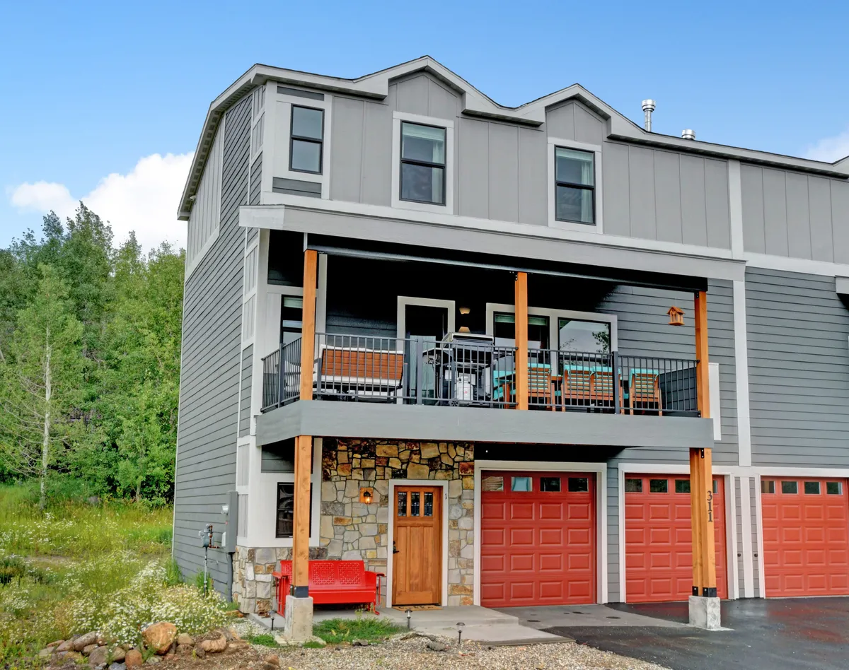 This image captures the exterior of the property, showcasing a welcoming balcony with comfortable seating, a stone entryway, a striking red bench, and garage doors. The balcony setting suggests a perfect spot for group relaxation and socializing, while the inviting entry emphasizes arrival and gathering.