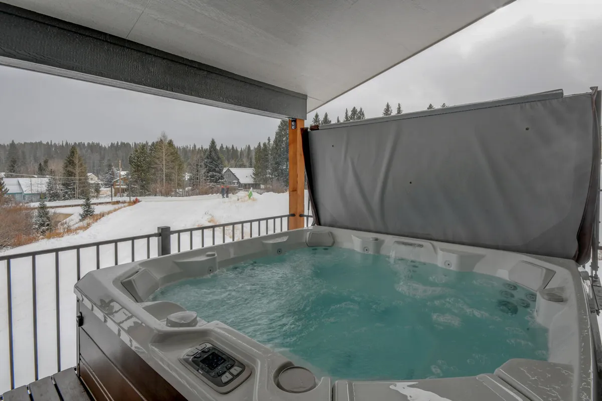 A serene scene featuring a hot tub on an outdoor deck, framed by a wooden railing and overlooking a snowy landscape. The space is perfect for unwinding after a day of adventure, with the potential for stargazing or group relaxation.
