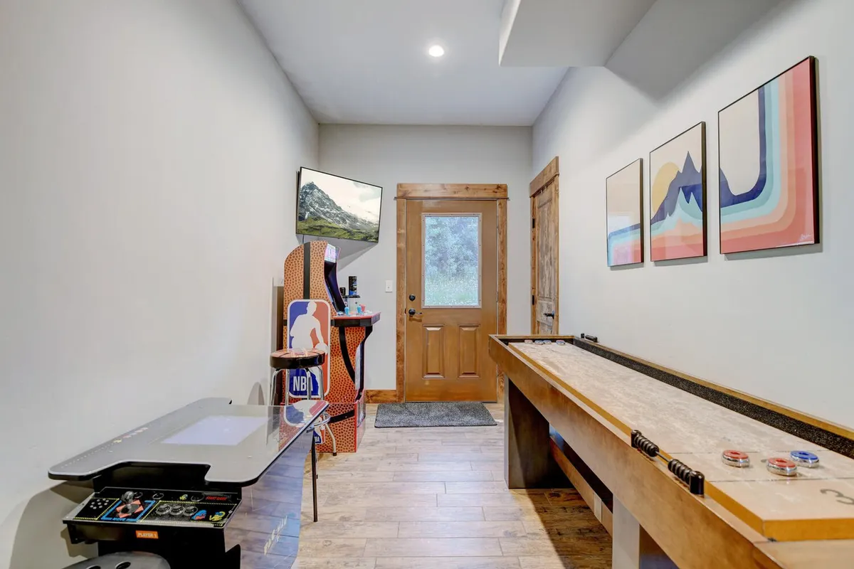 This interior image spotlights a lively game lounge with an arcade machine, shuffleboard table, colorful artwork, and a window offering mountain views. The space is filled with energy and is designed for playful group activities and friendly competition.