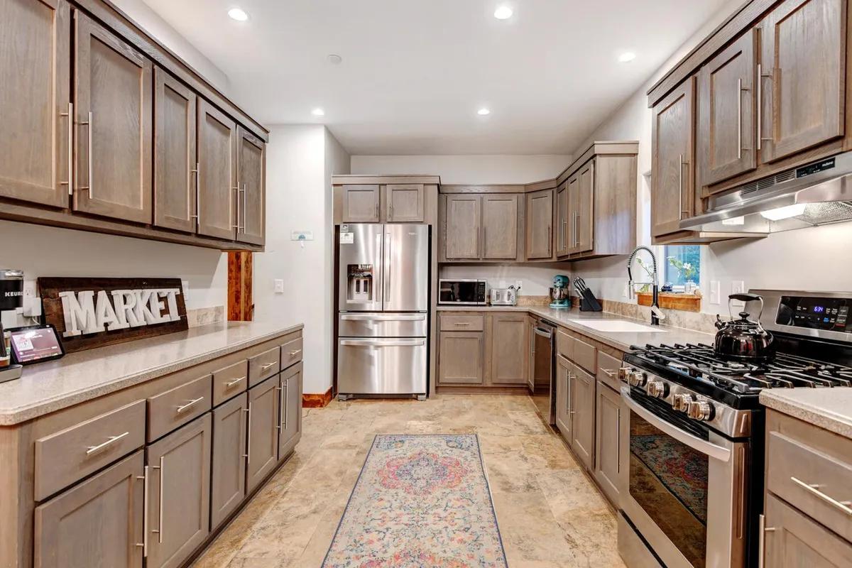 A bright and spacious kitchen featuring stainless steel appliances, granite countertops, and wooden cabinetry. A decorative rug adds warmth, and the arrangement encourages cooking, entertaining, and family interaction.