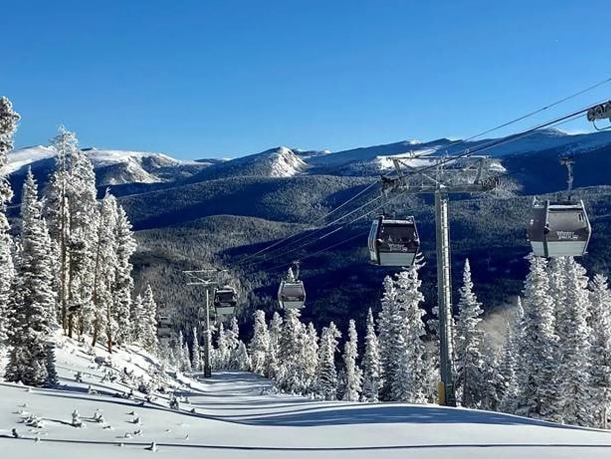A sweeping view of ski lift gondolas gliding over snow-covered slopes, with distant mountain peaks and tall pine trees creating a dramatic alpine backdrop. The scene captures the excitement of winter sports and the natural beauty of the Rockies.